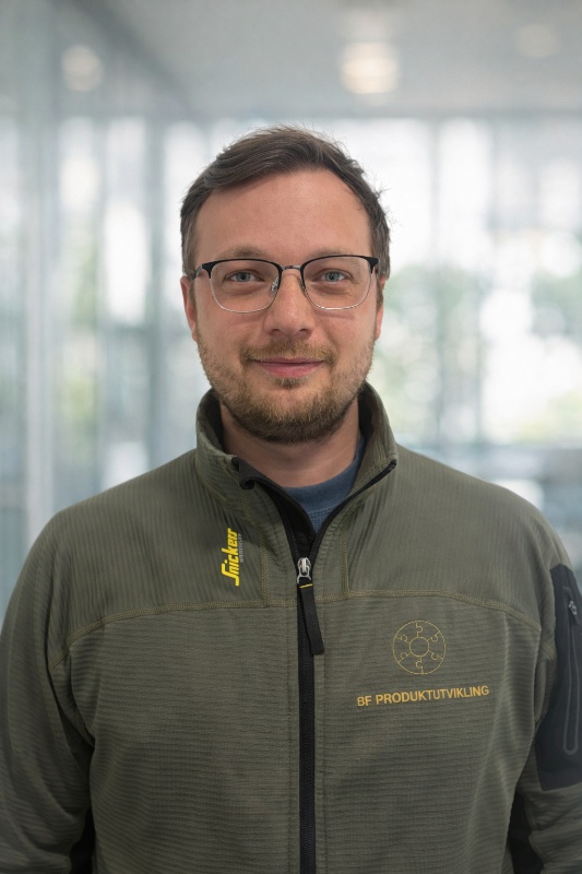 Mann med mørkt hår og briller i grønn jakke